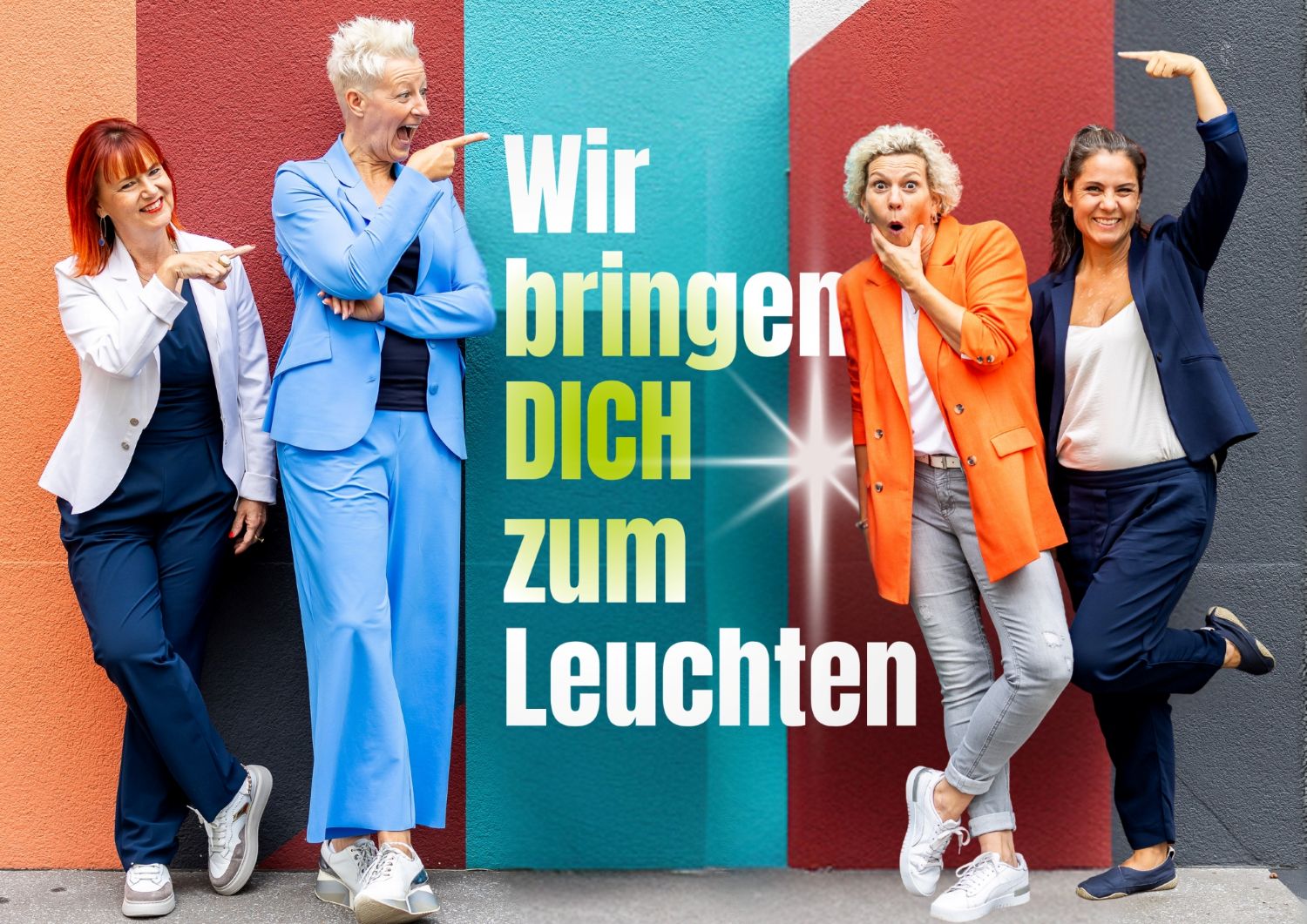 Das Team der Mind-In GmbH steht vor einer bunten Wand und macht lustige Posen. Auf der Wand steht der Unternehmensslogan: Wir bringen dich zum Leuchten.