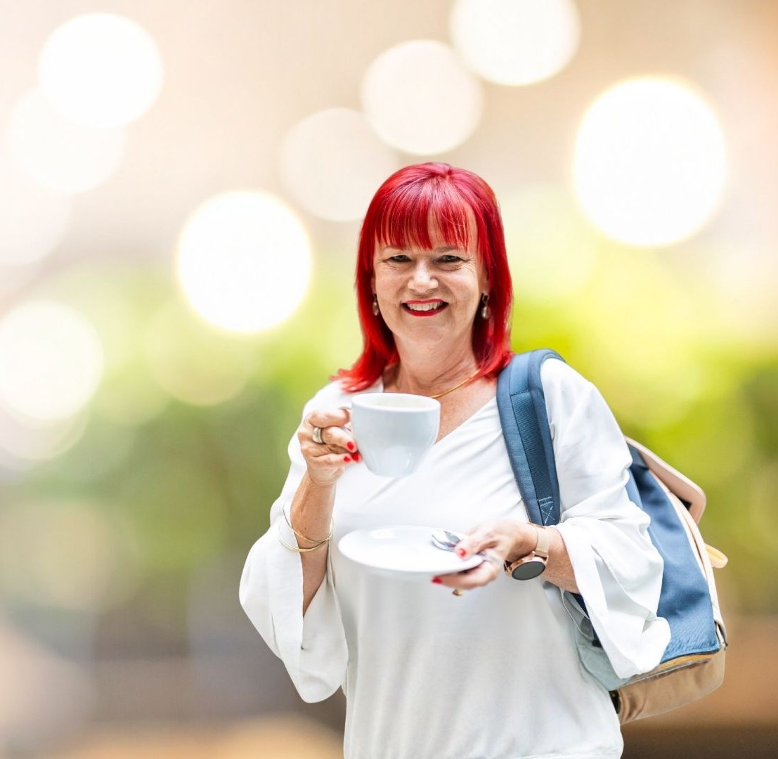 Eine Frau lächelt in die Kamera und hält einen Kaffee in der Hand
